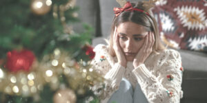 Woman looking sadly at Christmas tree, representing holiday grief