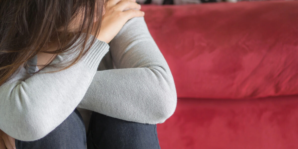 How do I cope with Grief? woman sitting on a red couch holding her knees, head resting on them, sad